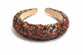 A wide, chunky headband covered in dense multicolor sequins and beads, resting on a dark wooden surface.