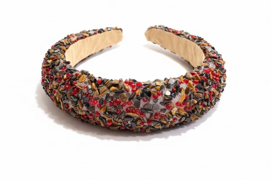A wide, chunky headband covered in dense multicolor sequins and beads, resting on a dark wooden surface.