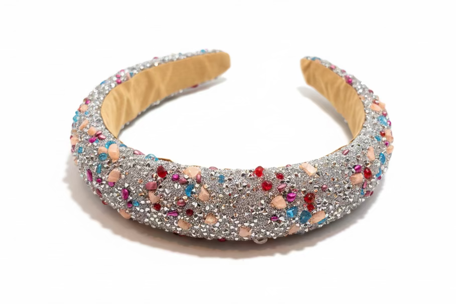 A glittery silver headband decorated with multicolored rhinestones, resting on a dark wooden surface.