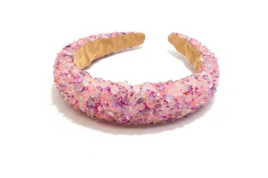A chunky open cuff headband covered in pink and purple glitter crystals, resting on a dark wooden surface.