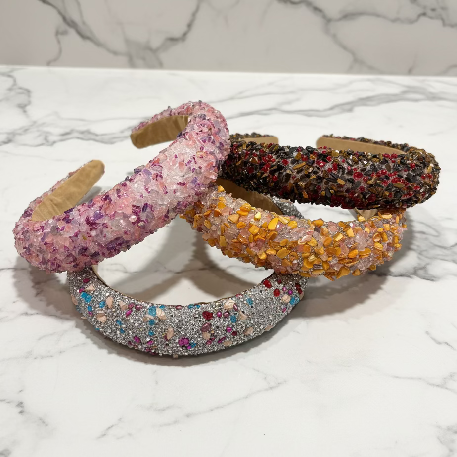Three handmade glitter headbands displayed on a dark wooden surface. The headbands are covered in dense, multi-colored glitter and feature a natural tan wood inner band.